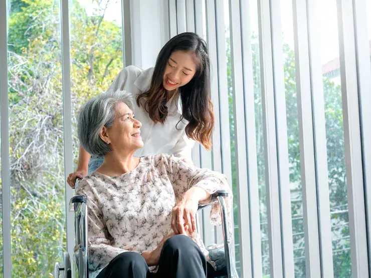 휠체어에 앉은 어르신과 미소 짓는 젊은 요양보호사